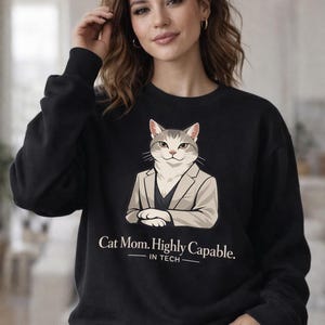 May include: Black sweatshirt featuring a cartoon cat in a blazer with the text "Cat Mom. Highly Capable. IN TECH." The cat is gray and white with a serious expression. The sweatshirt is a crew neck.