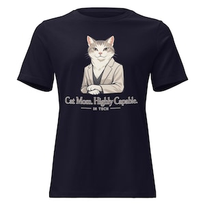 May include: Navy blue t-shirt featuring a cartoon cat wearing a blazer. The cat illustration is in shades of gray and white. Text on the shirt reads "Cat Mom. Highly Capable. IN TECH."