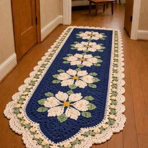 Puede incluir: Una alfombra de ganchillo rectangular, hecha a mano, con un centro azul marino y un diseño floral. La alfombra presenta grandes flores blancas con centros amarillos y hojas verdes, bordeada por un borde festoneado color crema. La alfombra está sobre un suelo de madera.