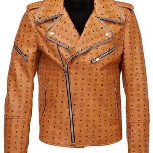 May include: A tan leather jacket with a black diamond pattern and silver zippers. The jacket has an asymmetrical zipper closure, a notched collar, and multiple pockets. The jacket is a classic biker style.
