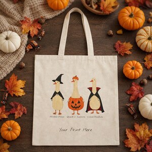 May include: A beige canvas tote bag featuring a graphic of three ducks in Halloween costumes with the text Honkus Pocus, Quack-o-Lantern, and Count Honkula, along with the phrase Your Print Here printed in black ink on the front of the bag.