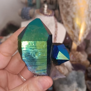 May include: A hand holding a large, iridescent quartz crystal with a vibrant green and blue sheen. The crystal has a rough, natural texture and a pointed, geometric shape. The crystal is a striking example of natural mineral formations.