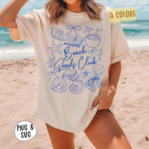 Op de afbeelding: Crèmekleurig T-shirt met een blauwe grafische afbeelding van schelpen, boeken en de tekst "Beach Reads Club". Het shirt heeft korte mouwen en een relaxte pasvorm, ideaal voor het strand. De afbeelding toont ook de tekst "PNG & SVG" en "5 COLORS".