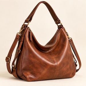 Pode incluir: Uma bolsa hobo de tamanho médio num tom castanho quente e rico com acabamento texturizado. Possui uma alça superior única, um compartimento principal com fecho de correr e tiras laterais ajustáveis com ferragens em tom de latão antigo.