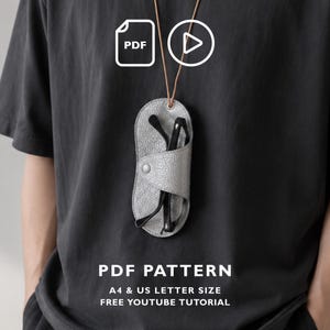 May include: A grey textured leather glasses case with a snap button closure, suspended by a thin brown cord. The image includes icons for PDF and video, with text reading PDF PATTERN, A4 & US LETTER SIZE, FREE YOUTUBE TUTORIAL.