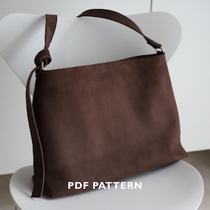 May include: A brown suede shoulder bag with a long strap, resting on a white chair. The bag has a rectangular shape and a simple design. The text "PDF PATTERN" is visible at the bottom of the image.