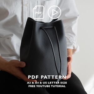 Puede incluir: Un bolso tipo cubo de color gris oscuro con superficie texturizada, cierre de cordón y costuras blancas en contraste. La imagen incluye el texto PDF PATTERN, A3 & A4 & US LETTER SIZE, FREE YOUTUBE TUTORIAL, junto con iconos de PDF y reproducción.