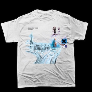 Puede incluir: Camiseta blanca con la ilustración del álbum "OK Computer" de Radiohead. El diseño presenta una escena de autopista azul y blanca, con el texto "OK COMPUTER" y "RADIOHEAD". También hay otros elementos gráficos.