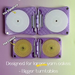 May include: Two purple folding yarn cake holders labelled The Signature and The Classic. The Signature features larger white circular turntables, while The Classic has smaller gold-toned turntables. Both include metal spindles and magnets.
