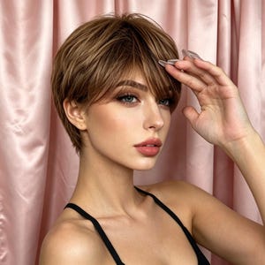 Peut inclure: Une femme aux cheveux courts, bruns clairs et en couches, avec des mèches et une frange. Elle porte un haut noir. Elle a la peau claire, les yeux bleus et du rouge à lèvres rose. Sa main est près de son front.