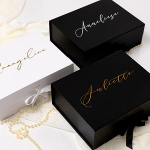 May include: Three rectangular gift boxes with magnetic closures and ribbon ties. One white box features the gold script name Evangeline. Two black boxes feature script names: one in silver reading Anneliese and one in gold reading Juliette.
