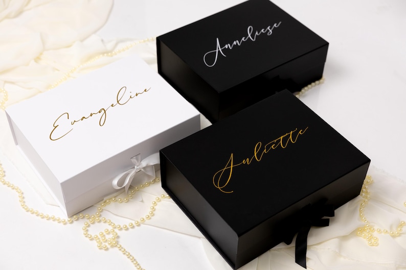 May include: Three rectangular gift boxes with magnetic closures and ribbon ties. One white box features the gold script name Evangeline. Two black boxes feature script names: one in silver reading Anneliese and one in gold reading Juliette.