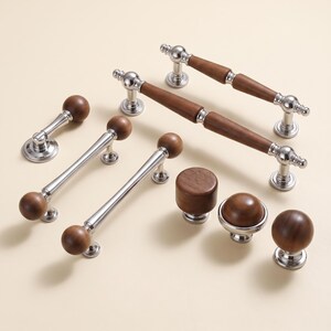 May include: A collection of cabinet hardware including several drawer pulls and knobs. Each piece features a combination of polished silver-tone metal bases and smooth, dark brown wooden accents, showcasing a mix of cylindrical and spherical shapes.
