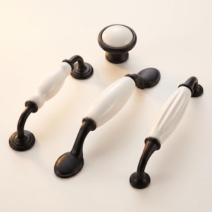 Op de afbeelding: Een set van vier meubelbeslagstukken, bestaande uit een ronde knop en drie verschillende ladehandgrepen. Elk item combineert een basis van matzwart metaal met een glanzend wit keramisch middengedeelte in diverse vormen.
