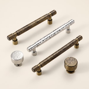 May include: A collection of cabinet hardware including three long bar pulls and two round knobs. The hardware features a hammered texture with two pieces in a polished silver finish and three pieces in an antique brass finish with dark accents.
