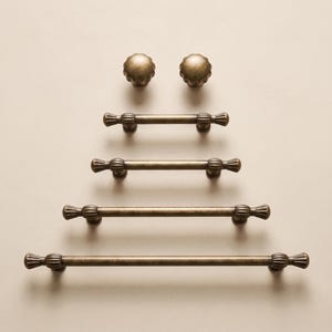 May include: A collection of antique brass hardware consisting of two round fluted knobs and four drawer pulls of varying lengths. Each pull features a central rod with fluted end caps and mounting posts, showcasing a consistent metallic finish.