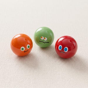 Könnte beinhalten: Drei glatte, kugelförmige Objekte in Orange, Grün und Rot. Jede Kugel ist mit einem Paar Comic-Augen und einer einfachen Linie als Mund versehen. Die orangefarbene Kugel hat grüne Augen, die grüne Kugel hat orangefarbene Augen und die rote Kugel hat blaue Augen.