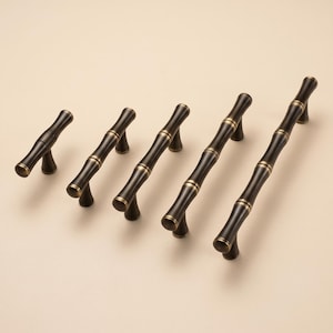 May include: Five cabinet pulls in a dark bronze finish with a bamboo-inspired design. Each handle features a segmented, cylindrical shape with raised rings at the joints and two sturdy mounting posts, arranged in increasing order of length.
