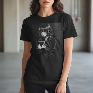 May include: Black t-shirt featuring a grayscale anime-style illustration of a person holding a book. The person has long hair in a braid. The shirt is a crew neck and appears to be made of cotton.