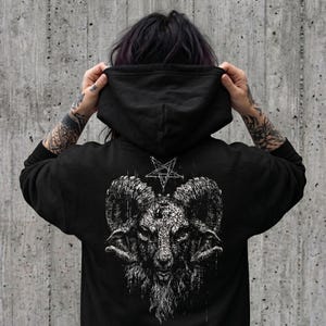 May include: A black hooded sweatshirt featuring a large, detailed white graphic on the back. The design depicts a ram head with curved horns and a pentagram symbol positioned directly above the animal's head, rendered in a dark, textured style.