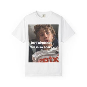 May include: White t-shirt featuring a photo of a person with the text "I love airplanes this is so scary". The person in the photo is wearing a white shirt with the word "201x" in red.