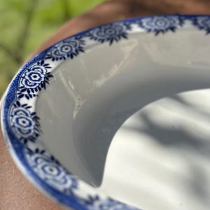 Könnte beinhalten: Eine weiße Keramikservierschale mit einem blauen Blumenmuster am Rand. Die Schale hat eine geschwungene Form und eine glänzende Oberfläche. Das blaue Blumendesign ist detailliert und aufwendig und verleiht einen Hauch von Eleganz.