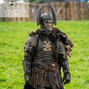 Puede incluir: Una armadura oscura completa con un casco con cuernos, usada por una persona de pie en un campo cubierto de hierba. La armadura incluye una placa para el pecho, protectores de hombros y protección para las piernas. El casco tiene una visera. El texto "Knights In" está incluido.