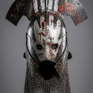 May include: A weathered metal helmet with a handprint design and blood splatter. The helmet features a visor, a chainmail neck guard, and a curved top. The image includes the text "KNIGHTS IN".