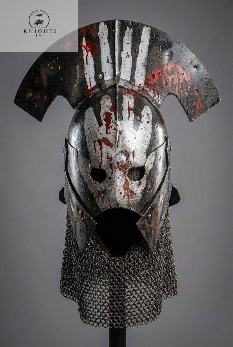 May include: A weathered metal helmet with a handprint design and blood splatter. The helmet features a visor, a chainmail neck guard, and a curved top. The image includes the text "KNIGHTS IN".