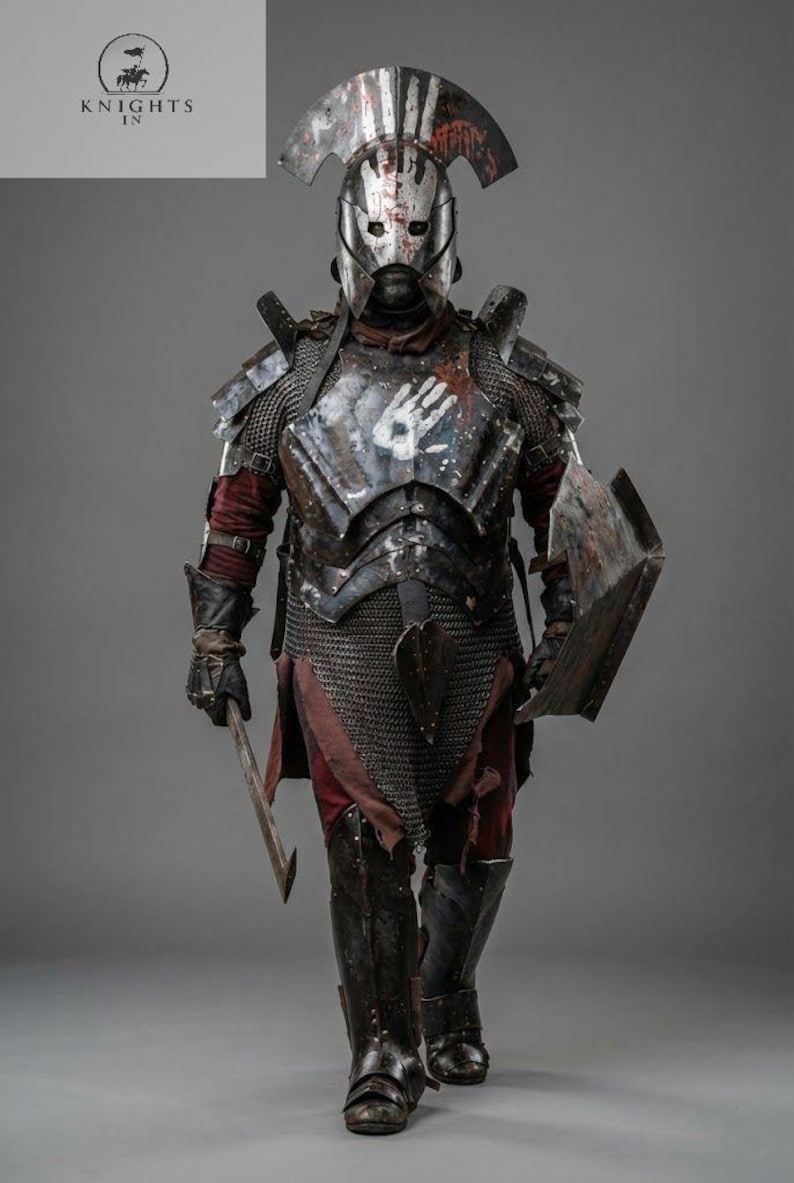 May include: A full-body shot of a medieval warrior in battle armor. The armor is a mix of metal and chainmail, with a helmet and shield. The chest plate has a white handprint. The warrior is holding a sword and shield.