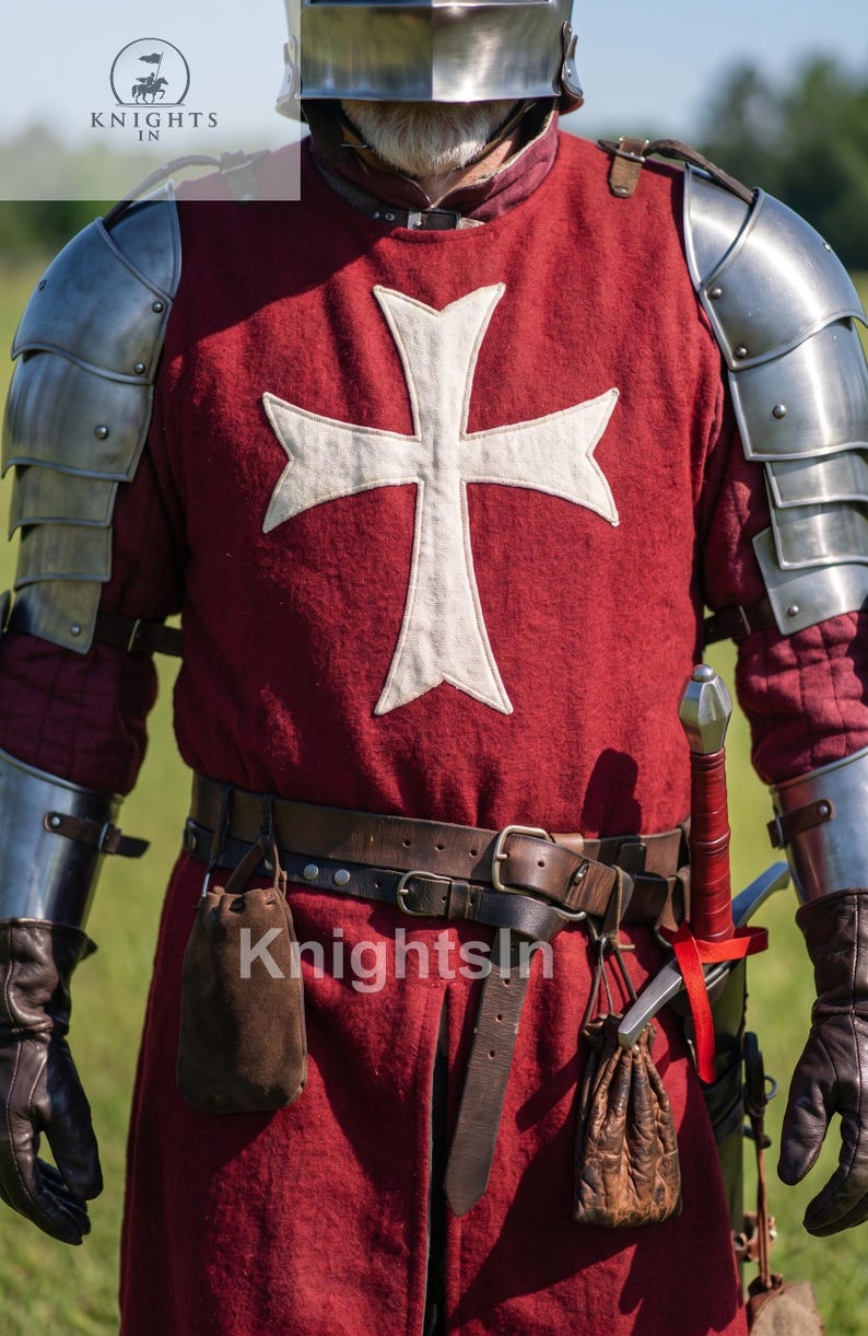 May include: A medieval knight's costume featuring a red tunic with a white cross emblem, metal armor, and a leather belt with pouches. The costume includes a sword and is labeled "Knights In".