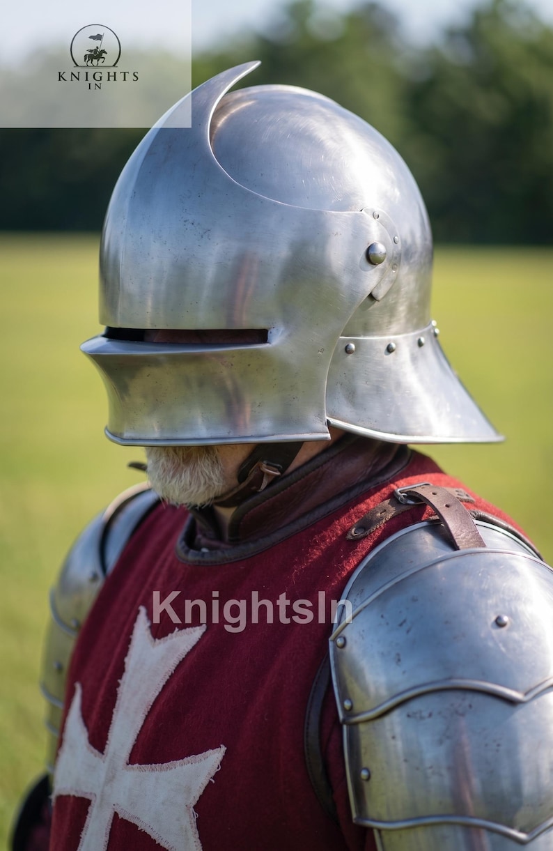May include: A polished steel helmet with a curved top and visor, part of a medieval knight's armor. The helmet is riveted and worn over a red tunic with a white cross emblem. The image includes the text "Knights In".