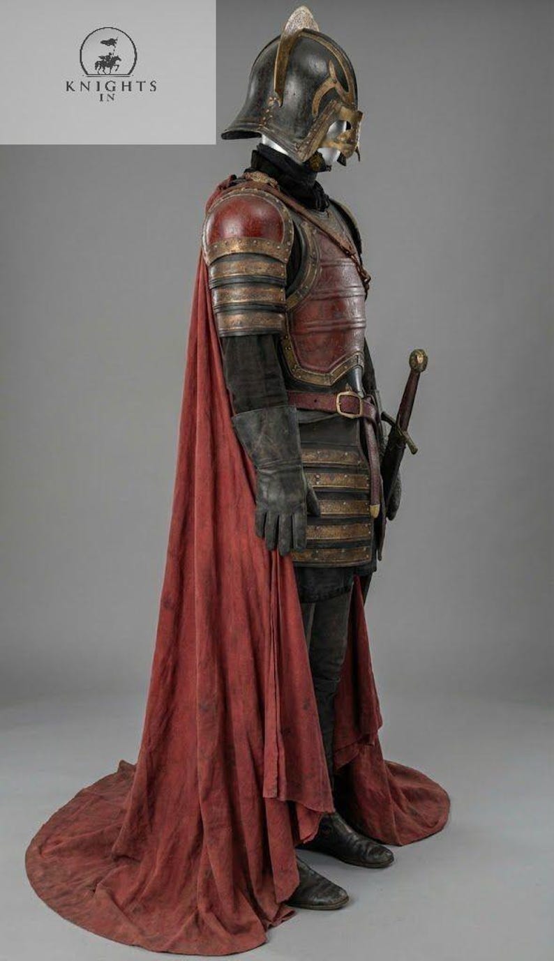 May include: A full suit of medieval armor, including a helmet, chest plate, and gauntlets. The armor is primarily dark red and gold, with a long red cape. A sword is sheathed at the waist. The image includes the text "KNIGHTS IN".