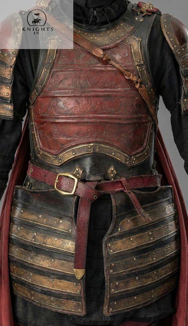 May include: Close-up of a medieval-style chest armor. The armor is primarily black with bronze-colored accents and a red leather belt. The chest plate has embossed detailing and is secured with a buckle. The Knights In logo is visible.
