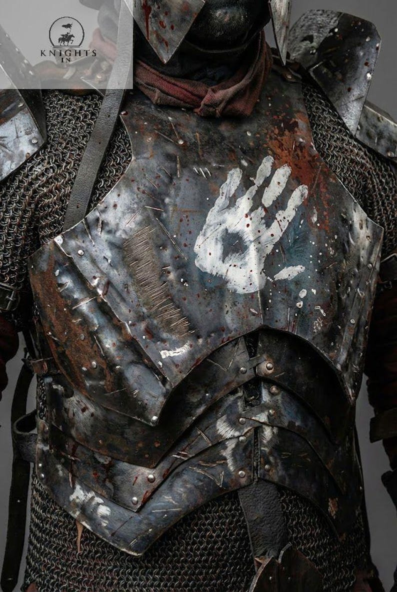 May include: Close-up of a weathered, dark metal breastplate with a white handprint. The armor shows signs of wear and tear, with rivets and layered plates. Chainmail is visible at the edges. The image includes the text "KNIGHTS IN".