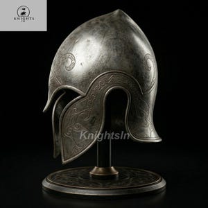 May include: A silver-colored helmet with intricate engraved designs, displayed on a black stand. The helmet features a pointed top and curved cheek guards. The base of the stand has a circular design. The text "Knights In" is visible.
