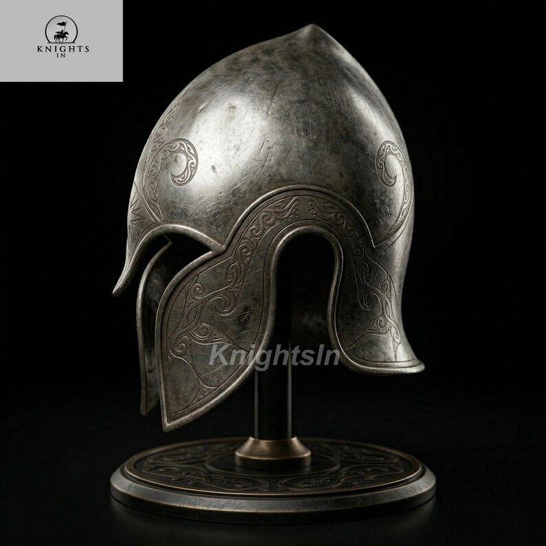 May include: A silver-colored helmet with intricate engraved designs, displayed on a black stand. The helmet features a pointed top and curved cheek guards. The base of the stand has a circular design. The text "Knights In" is visible.