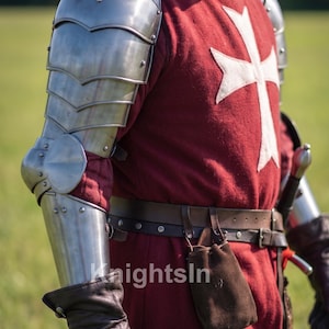 May include: A medieval knight's outfit featuring a red tunic with a white cross, metal armor, and leather gloves. The image includes the text "Knights In". The armor covers the shoulders and arms, with a belt and pouch at the waist.