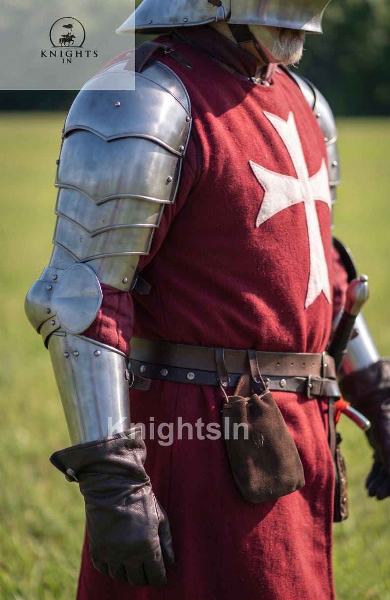 May include: A medieval knight's outfit featuring a red tunic with a white cross, metal armor, and leather gloves. The image includes the text "Knights In". The armor covers the shoulders and arms, with a belt and pouch at the waist.