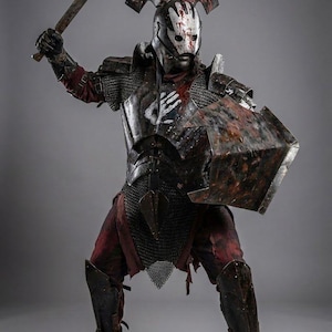 May include: A warrior in full armor, wielding a battle axe and shield. The costume features a helmet with a handprint design, chainmail, and distressed metal plating. The image includes the text "Knights In".