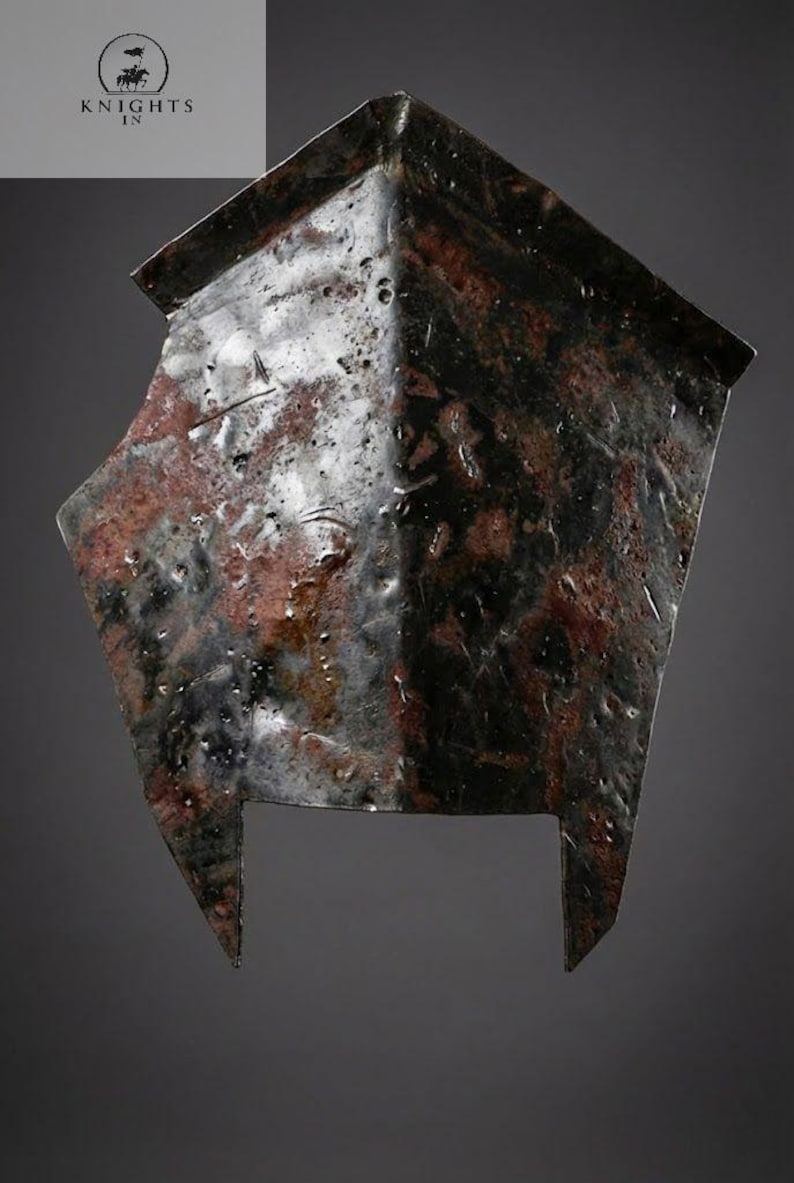 May include: A weathered, metal helmet with a dark, mottled finish. The helmet has a square top and two pointed extensions at the bottom. The surface shows signs of age and wear, with a mix of dark and reddish-brown tones. The logo "KNIGHTS IN" is in the upper left corner.