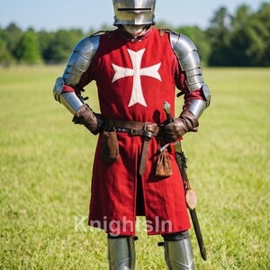 May include: A full suit of medieval armor, including a helmet, shoulder guards, and leg armor. The red tunic features a white cross. A sword hangs at the side. The image includes the text "Knights In".