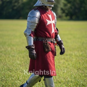 May include: A person in medieval armor, including a helmet, shoulder and arm protection, and leg guards, walks across a grassy field. The red tunic features a white cross. The image includes the text "Knights In".