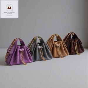 Może przedstawiać: Cztery zamszowe torby typu bucket w kolorze fioletowym, szarym, beżowym i brązowym, każda ze złotym łańcuszkiem i zamknięciem na sznurek. Torby ułożone są w rzędzie, prezentując swoje różne kolory i faktury. Logo Heritage Hide Studio znajduje się w lewym górnym rogu.