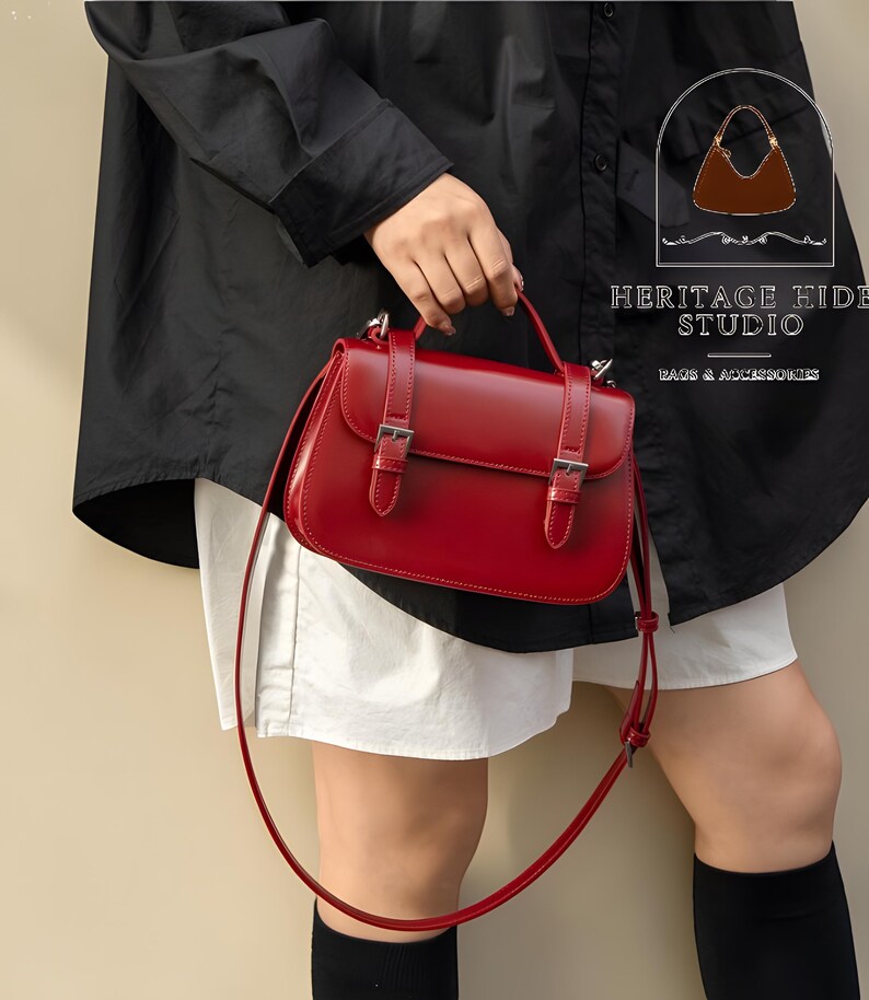Vintage genuine leather crossbody handbag with retro Cambridge satchel design displayed in elegant neutral studio setting. Women’s minimalist shoulder purse available in black, burgundy red, ivory white, and blush pink colors with structured silhouette, buckle strap details, top handle, and adjustable crossbody strap. Japanese style leather handbag styled for modern fashion lovers, classic British satchel aesthetic, everyday women’s purse, elegant casual shoulder bag