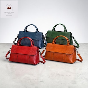May include: Four leather handbags in red, blue, green, and orange. Each bag has a top handle and a detachable shoulder strap. The flap features a textured, crocodile-like pattern. The bags are displayed on a light gray surface.