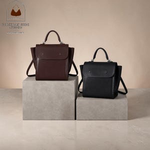 May include: Two structured handbags, one in dark brown and one in black, each featuring a top handle, a fold-over flap with two snap closures, and side gussets. The bags are displayed on separate grey blocks, showcasing a clean design.