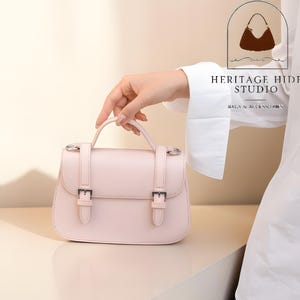 Vintage genuine leather crossbody handbag with retro Cambridge satchel design displayed in elegant neutral studio setting. Women’s minimalist shoulder purse available in black, burgundy red, ivory white, and blush pink colors with structured silhouette, buckle strap details, top handle, and adjustable crossbody strap. Japanese style leather handbag styled for modern fashion lovers, classic British satchel aesthetic, everyday women’s purse, elegant casual shoulder bag