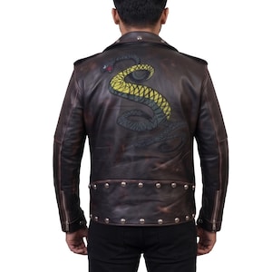 Könnte beinhalten: Eine dunkelbraune Lederjacke mit einer großen, gewundenen Schlangengrafik auf dem Rücken. Die Schlange ist in Gelb und Schwarz mit einer roten Zunge dargestellt. Die Jacke verfügt über einen breiten Kragen, silberfarbene Nieten am Saum und Reißverschlüsse.