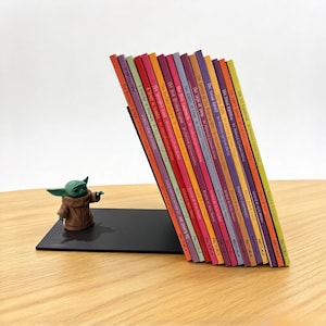 Peut inclure: Un serre-livres en métal noir avec une figurine de créature verte aux grandes oreilles vêtue d'une robe marron, soutenant une rangée de quinze livres fins et colorés, marqués Arcturus et écrits par Arthur Conan Doyle.